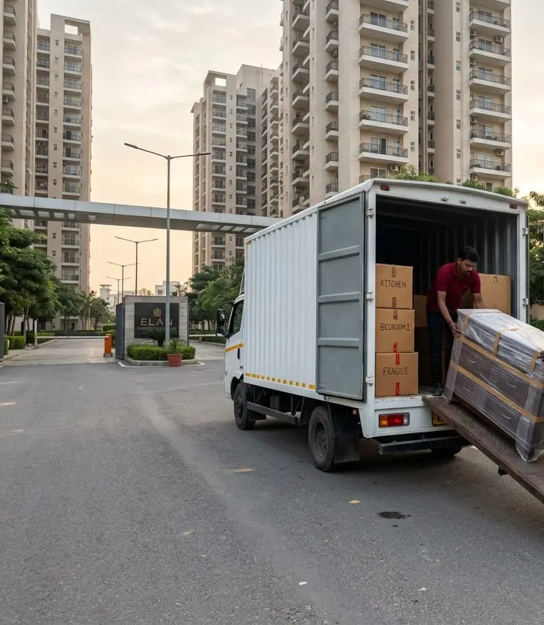 Packers in red uniforms loading wrapped furniture and labelled boxes into a moving truck outside a Greater Noida society